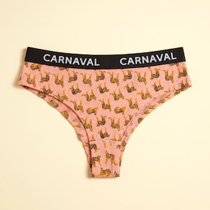 Op de afbeelding: Roze ondergoed met een herhalend tijgerpatroon en een zwarte elastische tailleband met de witte tekst CARNAVAL twee keer afgedrukt. Het kledingstuk heeft een hoog uitgesneden beenontwerp en een effen zwarte band.