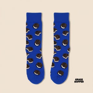 Könnte beinhalten: Ein Paar blaue Socken mit einem Muster aus Schokoladen-Sandwich-Keksen. Die Socken haben einen dunkelblauen Hintergrund und zeigen die Kekse in Braun und Weiß. Der Text "GRASSHOPPER" befindet sich in der unteren rechten Ecke.