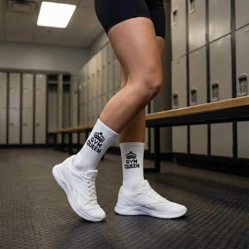 May include: A pair of white crew socks featuring a black crown graphic and the text "GYM QUEEN" printed on the upper calf area, worn with white athletic sneakers. The socks are ribbed and extend to the mid-calf, providing a clean look.