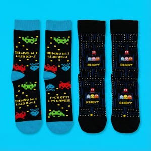 Könnte beinhalten: Vier Paar schwarze Socken mit Videospiel-Designs. Zwei Paare zeigen pixelige Alien-Grafiken und den Text "FACK OFF! I'M GAMING." Die anderen beiden zeigen ein von Pac-Man inspiriertes Design mit dem Wort "READY."