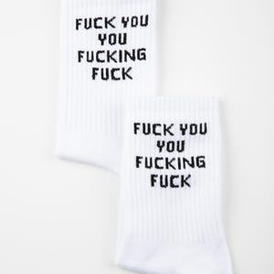 May include: Two white socks with the text "FUCK YOU YOU FUCKING FUCK" printed in black. The socks are ribbed and have a casual style. The brand name "GRASSHOPPER" is printed in the bottom right corner.