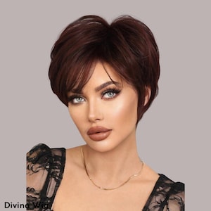 Puede incluir: Peluca corta de color castaño rojizo con capas y flequillo lateral. La peluca tiene un aspecto natural y está diseñada para enmarcar la cara. El texto "Divina Wig" es visible. Un peinado elegante.