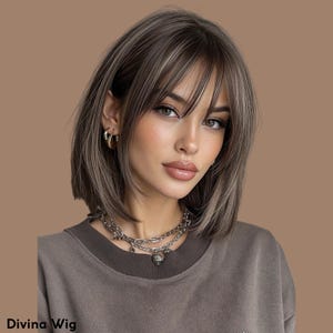 May include: A woman with a short, layered wig in shades of brown and blonde, styled with a fringe. She is wearing a brown top and a silver necklace. The text "Divina Wig" is at the bottom.
