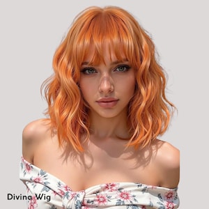Op de afbeelding: Een oranje pruik met golvend haar en pony. De pruik heeft losse krullen en een natuurlijke uitstraling. De tekst "Divina Wig" is linksonder zichtbaar.