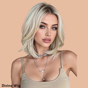 Può includere: Una parrucca bionda con un taglio a strati, lunghezza spalle. La parrucca ha una radice scura e un colore biondo chiaro. L'immagine mostra anche una donna che indossa una collana d'argento e un top beige. Il testo "Divina Wig" è in basso.