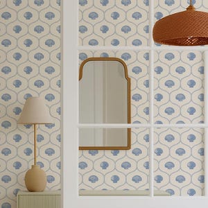 Op de afbeelding: Interieur van een eethoek met lichtblauw en wit behang met schelpmotief. Een ronde houten tafel en een lichtgroene bank zijn zichtbaar. Een ingelijste foto en een kleine lamp staan op een bijzettafel. De deur staat open.