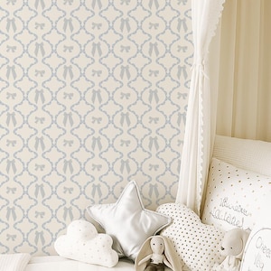 May include: A nursery scene with a cream-colored canopy bed and a patterned wallpaper. The wallpaper features a repeating light blue bow design. Decorative pillows, including star and cloud shapes, and stuffed animals complete the cozy setting.
