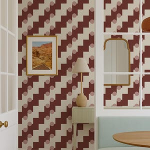 Puede incluir: Diseño de interiores con un comedor que incluye una mesa de madera, un banco azul claro y un papel pintado con motivos en burdeos y crema. Una obra de arte paisajística enmarcada cuelga de la pared y una lámpara descansa sobre una mesa auxiliar.