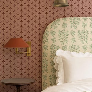 Può includere: Interno di una camera da letto con un letto con biancheria da letto bianca e bordo smerlato. La testiera ha un motivo floreale. Sono visibili anche un comodino e applique da parete con paralume rosso e finitura in ottone. La carta da parati ha un motivo a foglie ripetuto.