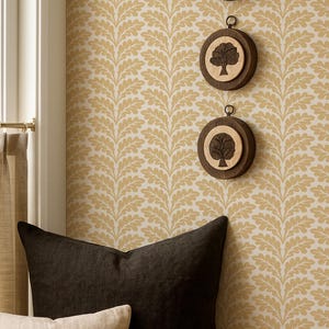 Może przedstawiać: Przytulne wnętrze z oknem, beżowymi zasłonami i wzorzystą tapetą. Wyeksponowano trzy drewniane, okrągłe dekoracje ścienne z motywami drzew. Dwie poduszki, jedna czarna i jedna beżowa, spoczywają na drewnianej powierzchni.