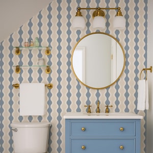 May include: A bathroom with a blue vanity, gold fixtures, and a round mirror. The walls are decorated with a blue and beige wavy pattern. A white toilet and a woven basket are also visible. A patterned rug adds a pop of color.