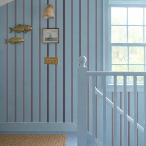 May include: A hallway with light blue walls featuring red vertical stripes. The decor includes gold fish ornaments, a framed picture of a sailboat, and a white staircase. A woven rug adds texture to the coastal interior.
