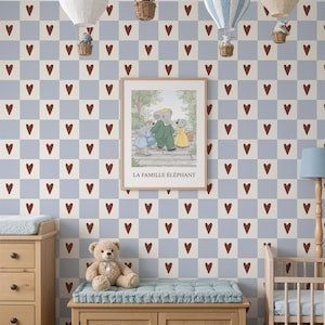 May include: A nursery with a blue and cream checkered heart wallpaper. The room features a wooden dresser, a bench with a teddy bear, a crib, and a blue toy car. Hot air balloons hang from the ceiling, and a framed print reads "LA FAMILLE ÉLÉPHANT."