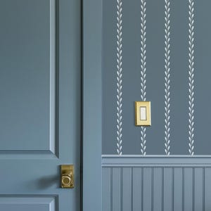 Può includere: Una porta blu con una maniglia dorata è a sinistra. Il muro è dipinto di blu con strisce verticali bianche a motivi di foglie. Un interruttore della luce dorato è montato sulla parete.