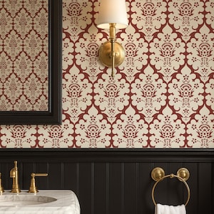 以下が含まれることがあります： 大理石の洗面台、金色の金具、金色のタオルリングに白いタオルが置かれたバスルームのインテリア。壁はクリーム色とバーガンディ色の模様の壁紙で、黒い腰壁があります。白いシェードのウォールスコンスが見えます。