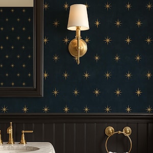 Puede incluir: Un baño con papel pintado azul oscuro con estampado de estrellas doradas, un lavabo de mármol blanco y paneles negros. Los accesorios dorados incluyen un toallero, un aplique de pared y un grifo. Una toalla blanca cuelga del anillo.