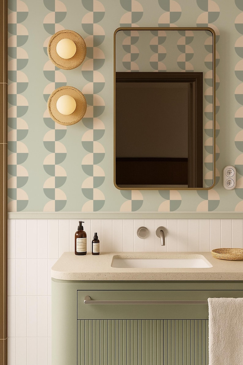 May include: A bathroom scene featuring a sage green vanity with a white sink and a gold-framed mirror. The wall has a geometric pattern in light blue and pink. Two woven sconces with round lights are mounted on the wall.
