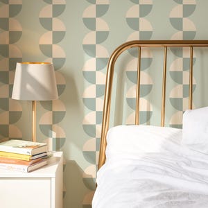 May include: A bedroom scene featuring a gold metal bed frame, a white nightstand with books, and a lamp. The wall is decorated with a repeating pattern of half-circle shapes in muted green and cream colors. The bed has white bedding.