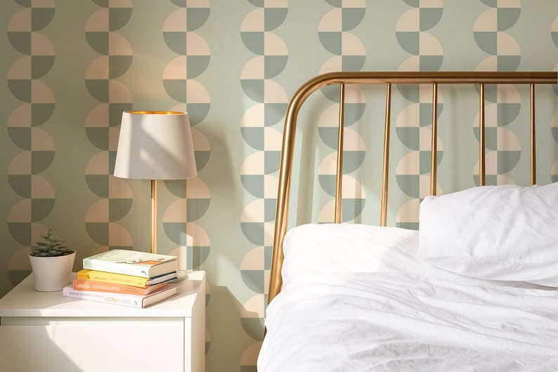 May include: A bedroom scene featuring a gold metal bed frame, a white nightstand with books, and a lamp. The wall is decorated with a repeating pattern of half-circle shapes in muted green and cream colors. The bed has white bedding.
