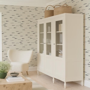 K&ouml;nnte beinhalten: Heller, luftiger Wohnraum mit einem wei&szlig;en Schrank mit Glast&uuml;ren, gekr&ouml;nt von zwei Weidenk&ouml;rben. Ein cremefarbener Sessel und ein Holztisch mit einer Pflanze und einer Schale sind ebenfalls vorhanden. Die W&auml;nde sind mit einem Fischmuster verziert.