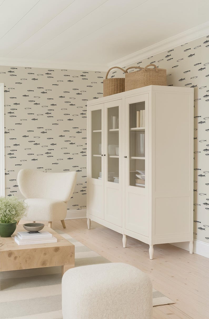 K&ouml;nnte beinhalten: Heller, luftiger Wohnraum mit einem wei&szlig;en Schrank mit Glast&uuml;ren, gekr&ouml;nt von zwei Weidenk&ouml;rben. Ein cremefarbener Sessel und ein Holztisch mit einer Pflanze und einer Schale sind ebenfalls vorhanden. Die W&auml;nde sind mit einem Fischmuster verziert.