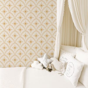 May include: Wallpaper featuring a repeating pattern of gold starbursts within arched, dotted outlines on a white background. A white bed is adorned with a star-shaped pillow, a cloud-shaped pillow, a heart-shaped pillow, and a square pillow with text.