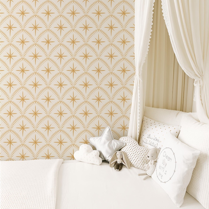 May include: Wallpaper featuring a repeating pattern of gold starbursts within arched, dotted outlines on a white background. A white bed is adorned with a star-shaped pillow, a cloud-shaped pillow, a heart-shaped pillow, and a square pillow with text.