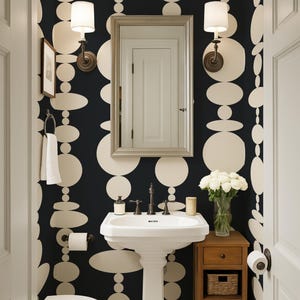 Pode incluir: Um lavabo com papel de parede de fundo preto e grandes formas circulares e ovais na cor creme. O ambiente inclui uma pia de pedestal branca, um espelho retangular, duas lumin&aacute;rias de parede, um vaso sanit&aacute;rio e um m&oacute;vel de madeira.