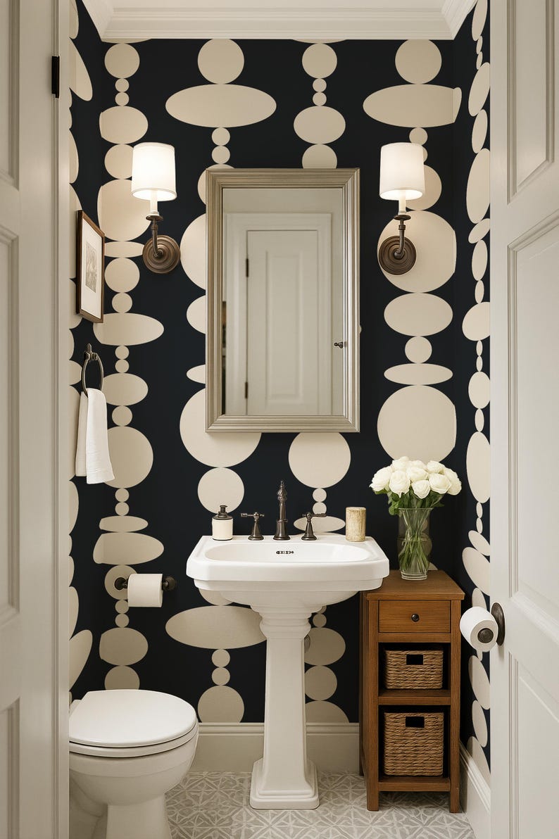 Pode incluir: Um lavabo com papel de parede de fundo preto e grandes formas circulares e ovais na cor creme. O ambiente inclui uma pia de pedestal branca, um espelho retangular, duas lumin&aacute;rias de parede, um vaso sanit&aacute;rio e um m&oacute;vel de madeira.