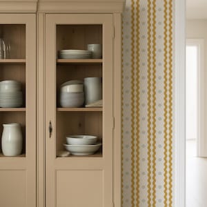 May include: A beige cabinet with glass doors displays white dishes and ceramic items. A woven basket sits atop the cabinet. The wall features a cream-colored wallpaper with vertical wavy yellow stripes and small gray floral accents.