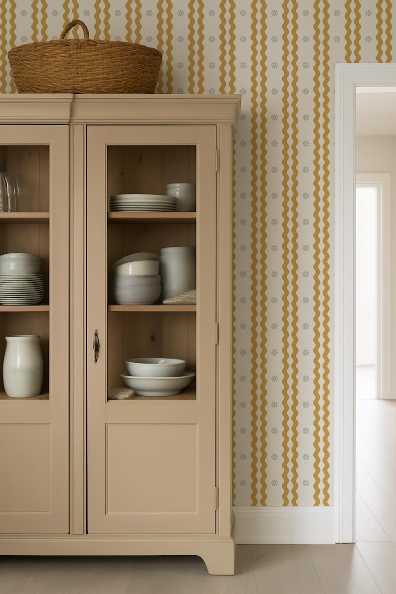 May include: A beige cabinet with glass doors displays white dishes and ceramic items. A woven basket sits atop the cabinet. The wall features a cream-colored wallpaper with vertical wavy yellow stripes and small gray floral accents.