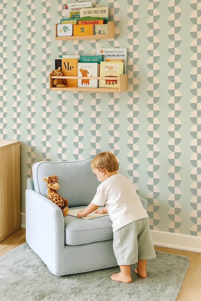 May include: A child's room with a light blue armchair, a giraffe stuffed animal, and a child looking at a book. The room has a light green and white patterned wallpaper and wooden bookshelves with children's books.