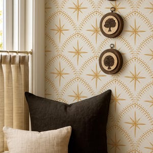 May include: Three circular wooden wall hangings featuring dark brown frames and light wood centers, two of which display a tree silhouette. These are mounted on a wall with a cream and gold starburst pattern, positioned above a dark and light pillow.