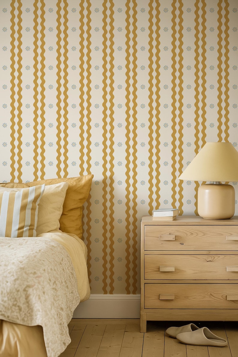 May include: A bedroom scene featuring a bed with yellow bedding and striped pillows. The wall is decorated with a cream-colored wallpaper with vertical wavy mustard-yellow stripes and small gray floral accents. A wooden nightstand and lamp complete the scene.