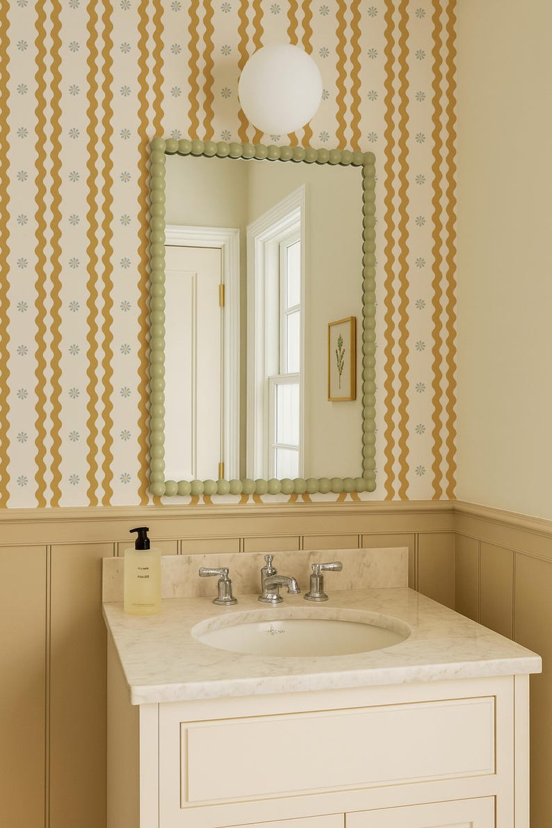 May include: A bathroom vanity with a marble countertop and a white sink. A green-framed mirror with a beaded edge hangs above the sink. The wall is decorated with a yellow and white wavy pattern wallpaper. A round white light fixture is mounted on the ceiling.