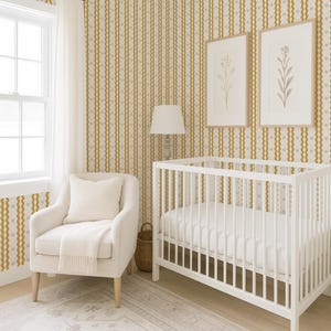 May include: A nursery room with a white crib, armchair, and a patterned rug. The walls are decorated with vertical stripes in gold and gray. Two framed botanical prints hang above the crib. A woven lampshade and a floor lamp complete the decor.
