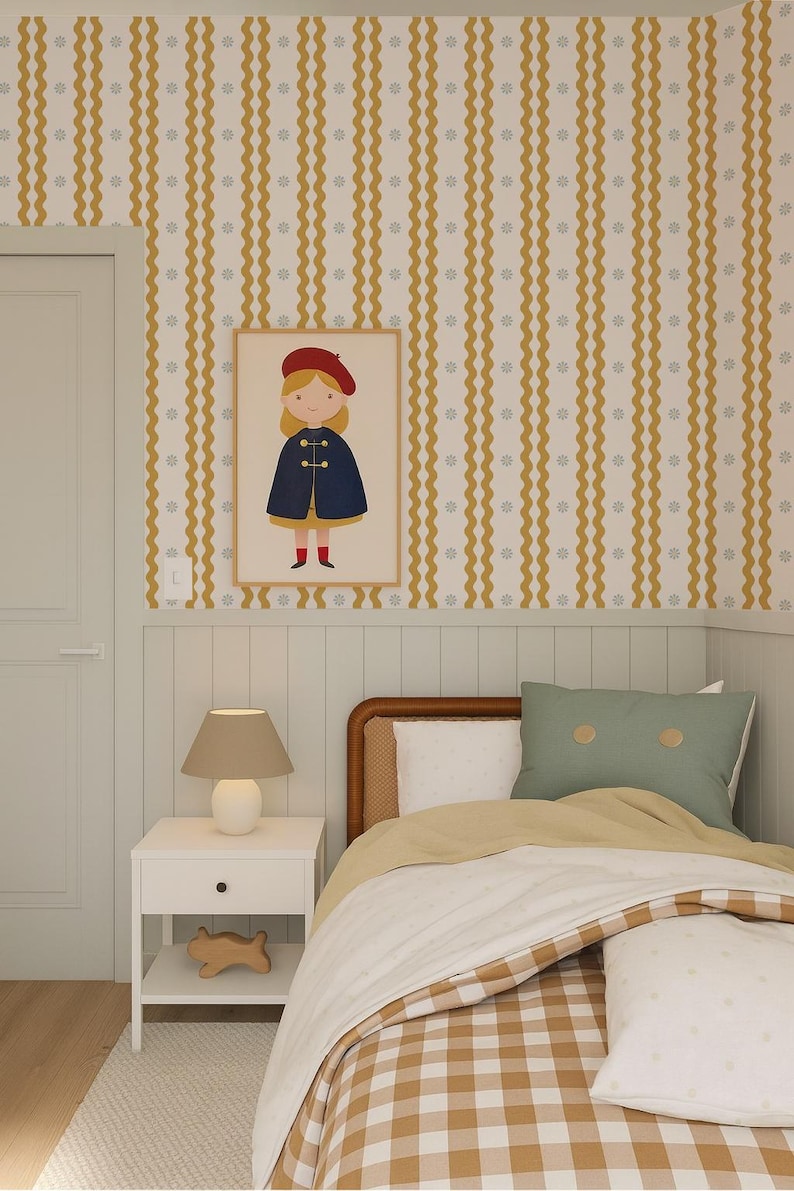May include: A child's bedroom with a framed illustration of a girl in a red beret and blue cape. The room features a bed with a checkered comforter, a white nightstand with a lamp, and yellow and white striped wallpaper.