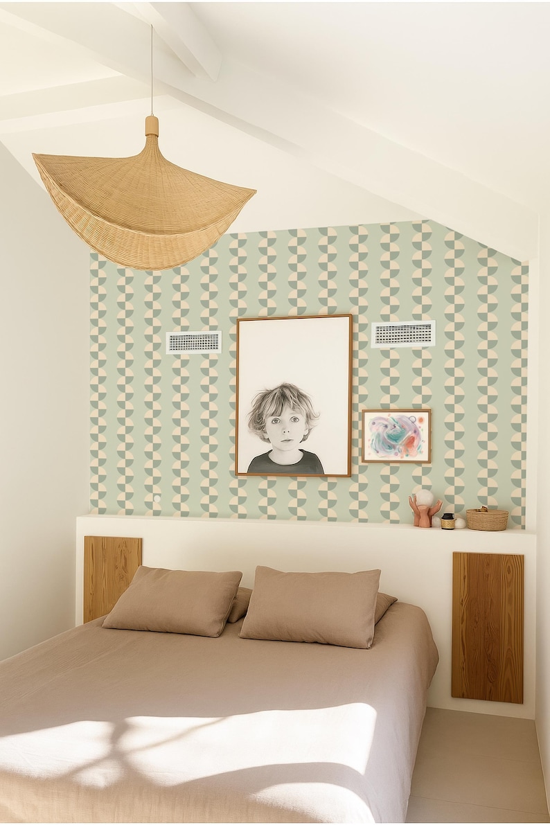 May include: Bedroom interior with a bed, pillows, and a neutral-toned duvet. The wall features a geometric pattern wallpaper and framed artwork. A woven pendant light hangs from the ceiling, and a small shelf displays decorative items.