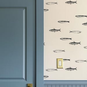 K&ouml;nnte beinhalten: Ein Raumabschnitt mit einer blauen T&uuml;r und einer Wand, die mit einem Fischmuster verziert ist. Die T&uuml;r hat einen goldfarbenen Griff. Die Wand hat einen cremefarbenen Hintergrund mit schwarzen Fischillustrationen.