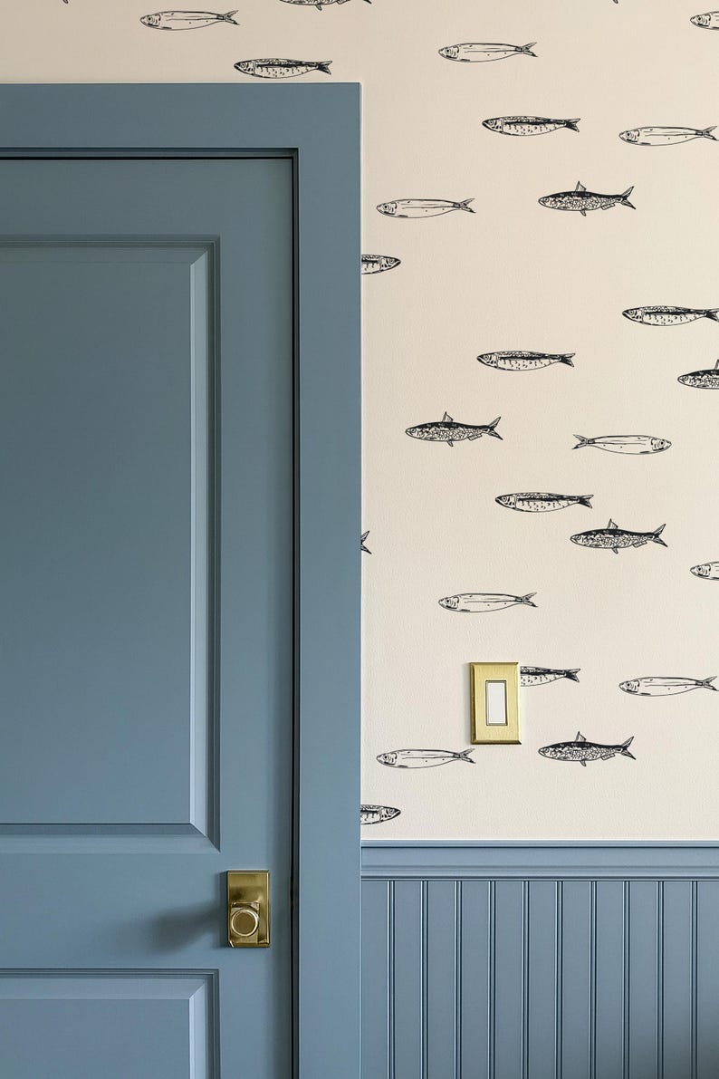K&ouml;nnte beinhalten: Ein Raumabschnitt mit einer blauen T&uuml;r und einer Wand, die mit einem Fischmuster verziert ist. Die T&uuml;r hat einen goldfarbenen Griff. Die Wand hat einen cremefarbenen Hintergrund mit schwarzen Fischillustrationen.