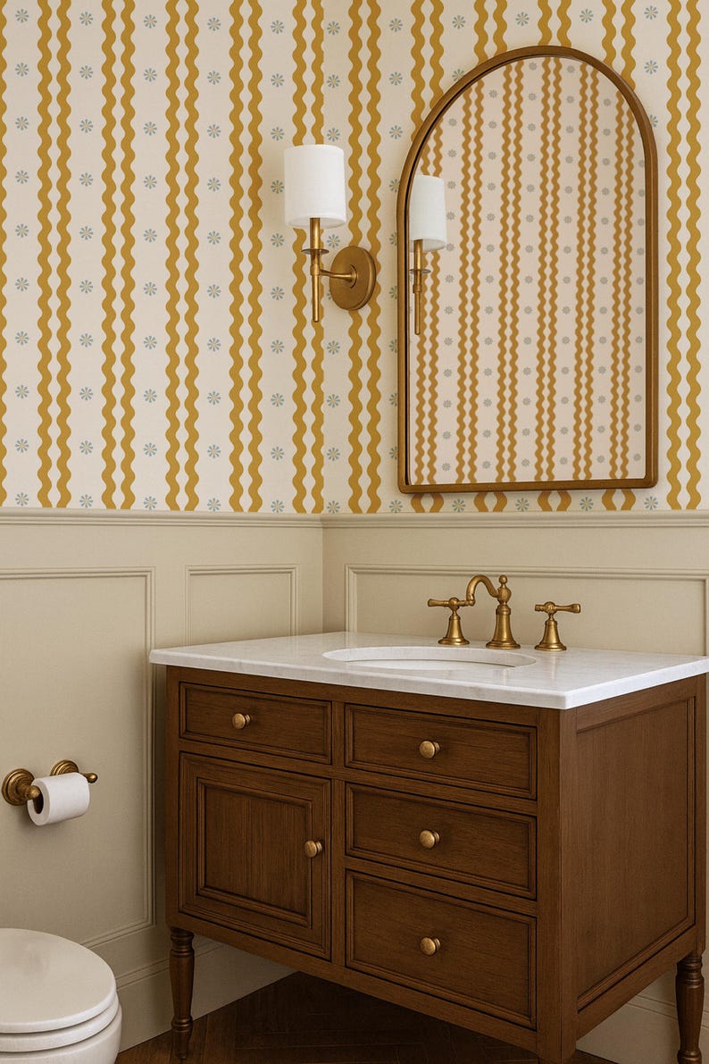 May include: A bathroom interior featuring a dark wood vanity with a white marble countertop and gold fixtures. The walls are decorated with a cream-colored wallpaper with yellow wavy stripes and small gray floral accents. A gold-framed mirror and sconces complete the space.