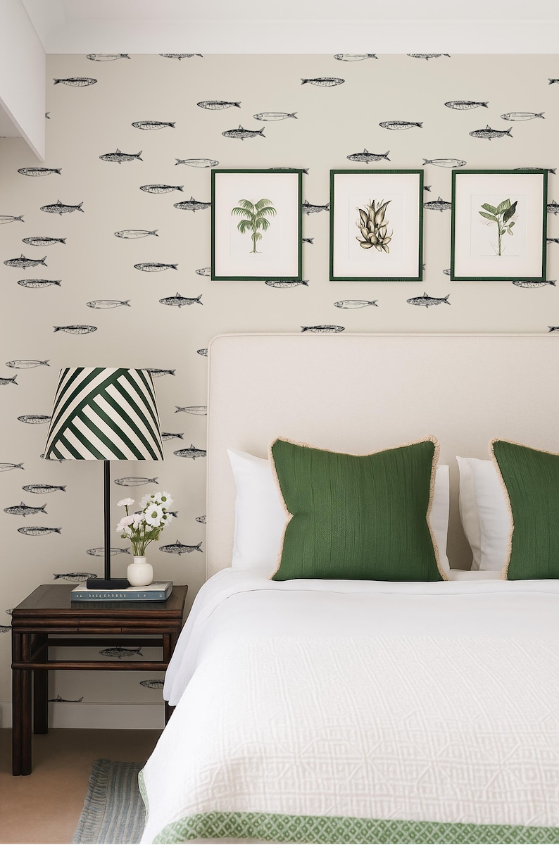 K&ouml;nnte beinhalten: Schlafzimmer-Interieur mit einem Bett mit wei&szlig;er Bettw&auml;sche und gr&uuml;nen Kissen. Die Wand ist mit einem Fischmuster und gerahmten botanischen Drucken verziert. Eine gestreifte Lampe und ein Nachttisch aus dunklem Holz sind ebenfalls zu sehen.