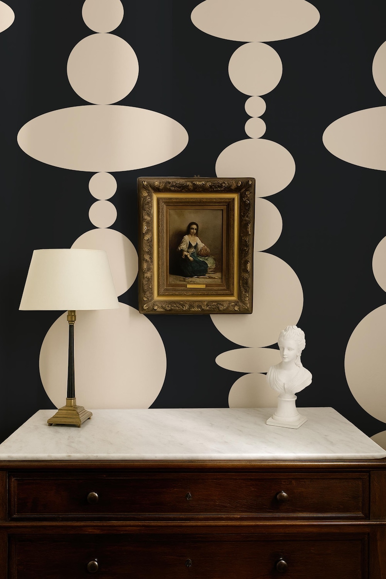 Pode incluir: Uma c&oacute;moda de madeira escura com tampo de m&aacute;rmore branco, um candeeiro de mesa com abajur creme, uma pintura a &oacute;leo emoldurada de uma figura sentada e um busto branco. A parede tem papel de parede preto com um padr&atilde;o de grandes c&iacute;rculos creme.