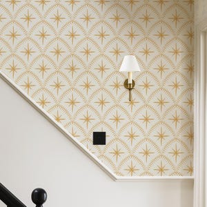 May include: Wallpaper featuring a repeating pattern of gold starbursts enclosed within arched, dotted lines on a white background. A wall-mounted light fixture with a white conical shade and a brass base is attached to the wall.
