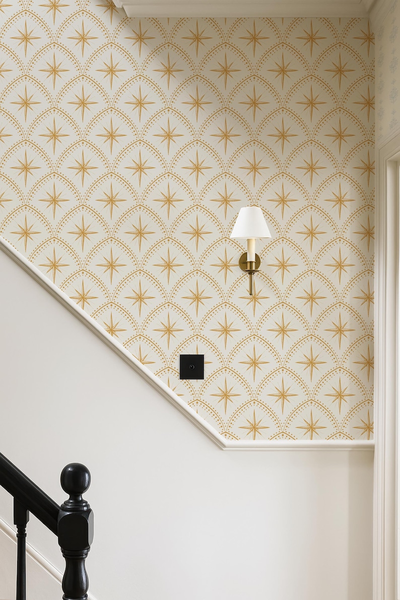 May include: Wallpaper featuring a repeating pattern of gold starbursts enclosed within arched, dotted lines on a white background. A wall-mounted light fixture with a white conical shade and a brass base is attached to the wall.