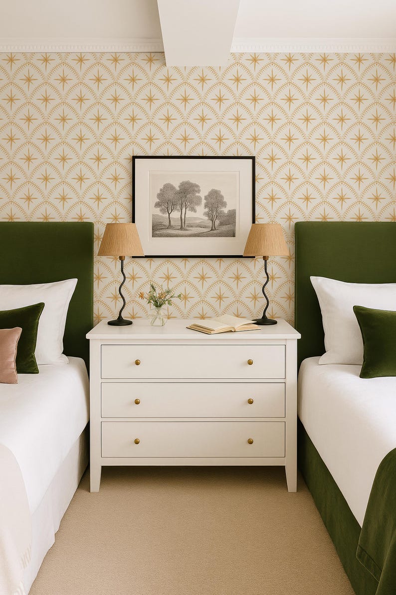 May include: A white three-drawer dresser with gold knobs sits between two beds with green velvet headboards. Two lamps with wavy black bases and pleated tan shades flank a framed black and white landscape print on the patterned wallpaper.