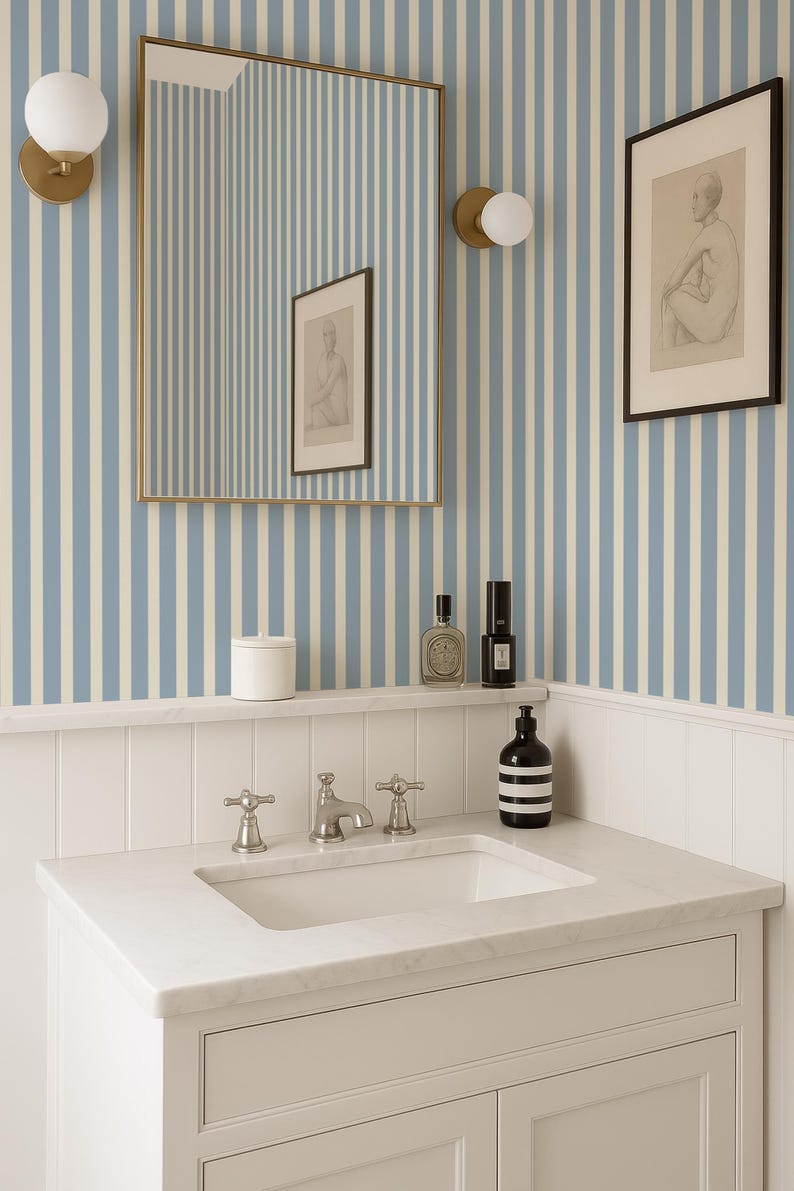 May include: A bathroom interior with a white marble vanity and chrome taps. The walls are decorated with blue and white striped wallpaper. A framed picture and a mirror are mounted above the vanity, alongside a shelf with toiletries.