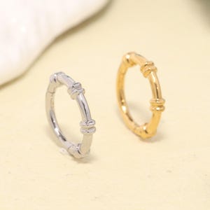 May include: Two circular rings, one in a polished silver tone and one in a polished gold tone. Each ring features a smooth, thin band accented with three distinct, raised decorative segments spaced evenly around the circumference of the metal hoop.