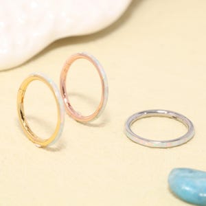 May include: Three circular hoop rings featuring an inlay of iridescent white opal. One ring is gold-toned, one is rose gold-toned, and one is silver-toned. Each ring has a thin, smooth metal band with a hinged closure mechanism for secure fastening.