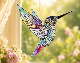 May include: A stained glass hummingbird suncatcher featuring a mosaic pattern of iridescent colors including purple, blue, yellow, and green. The bird is depicted in flight with wings extended, suspended by a thin silver chain from above.